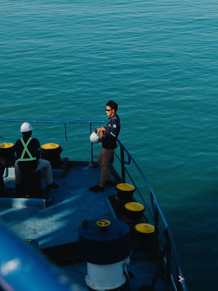 Two crew members on a ship deck, wearing safety gear, against the backdrop of the Indonesian sea.